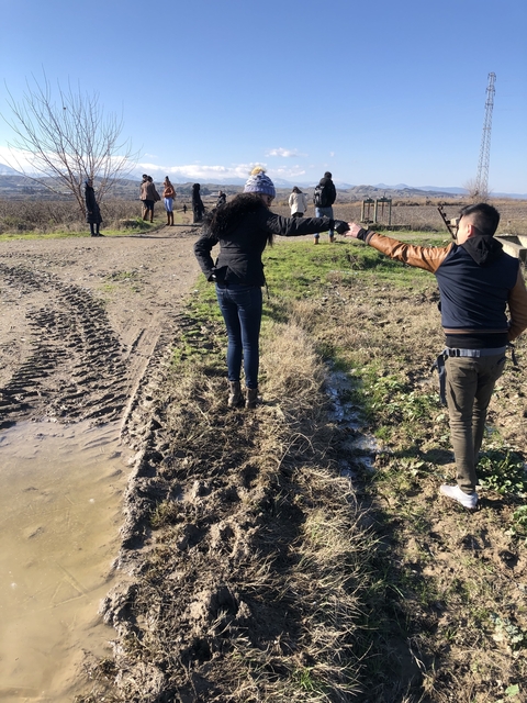 People holding hands to cross a muddy path in a countryside setting.