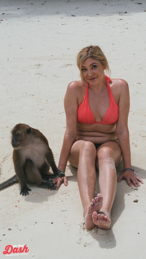 Woman sitting on a beach with a monkey beside her.