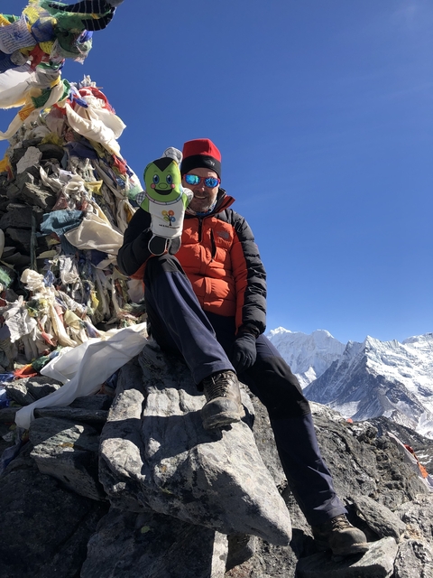Person posing with a cartoon cutout, snow-capped peaks in the background.