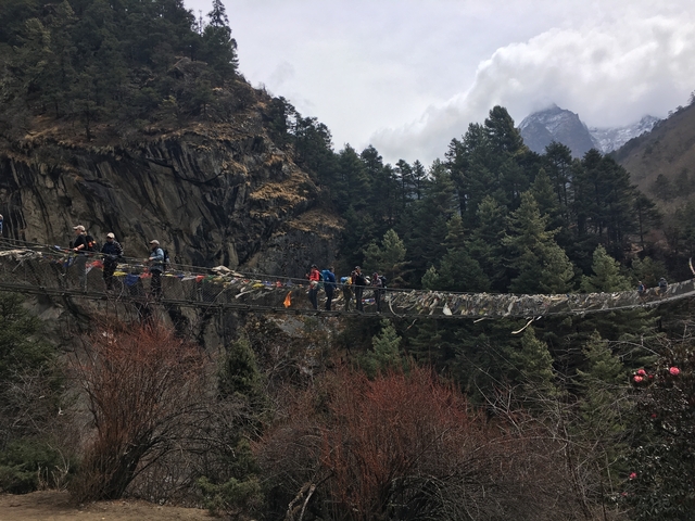 People crossing a suspension bridge in a mountainous area.