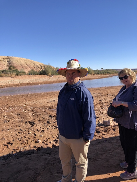 Two people standing by a river with red hills in the background.