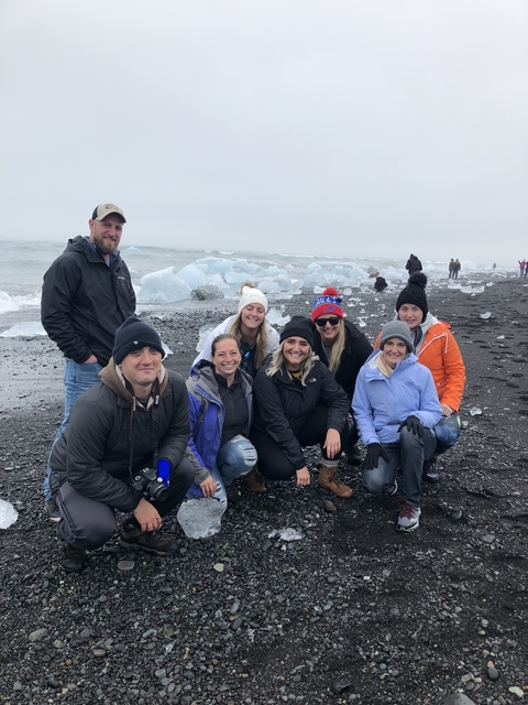 Group of people posing on a black sand beach with icebergs.