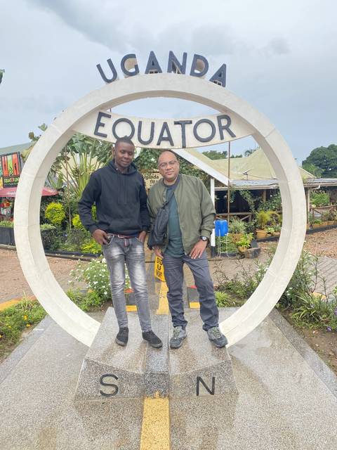       Two people standing at the Uganda Equator landmark.
  