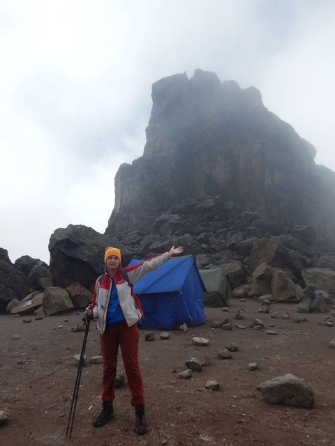       Person gesturing towards a rocky mountain with tents at the base.
  