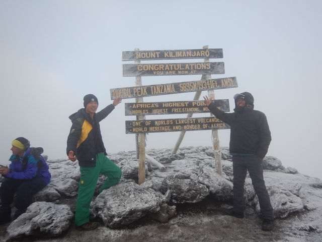       Hikers celebrating at the Uhuru Peak sign in snowy conditions.
  