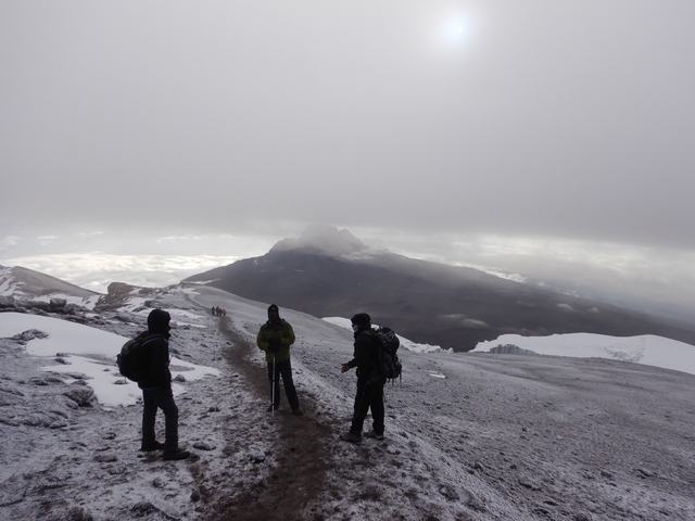       Hikers walking along a snowy path with mountains in the background.
  