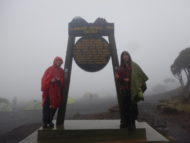       Two people standing in the fog at Shira Cave Camp sign.
  