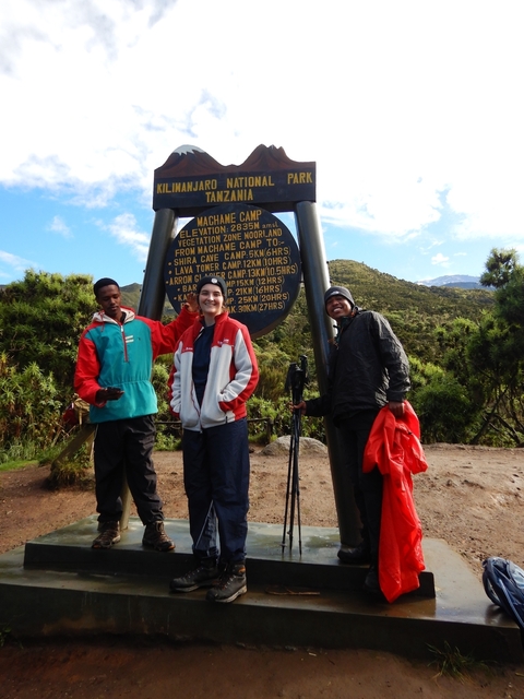       Three hikers at Machame Camp sign.
  