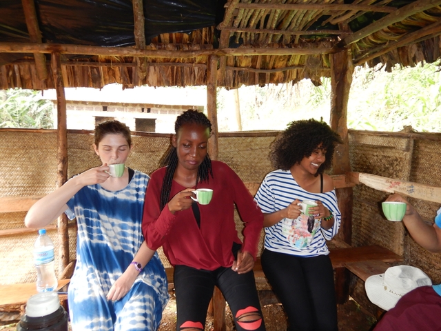       People sitting in a hut holding cups and smiling.
  