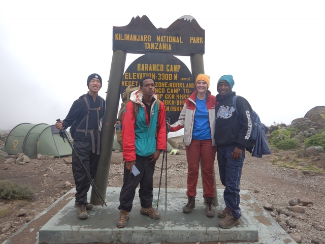       Group of friends smiling in front of a camp sign with tents around.
  