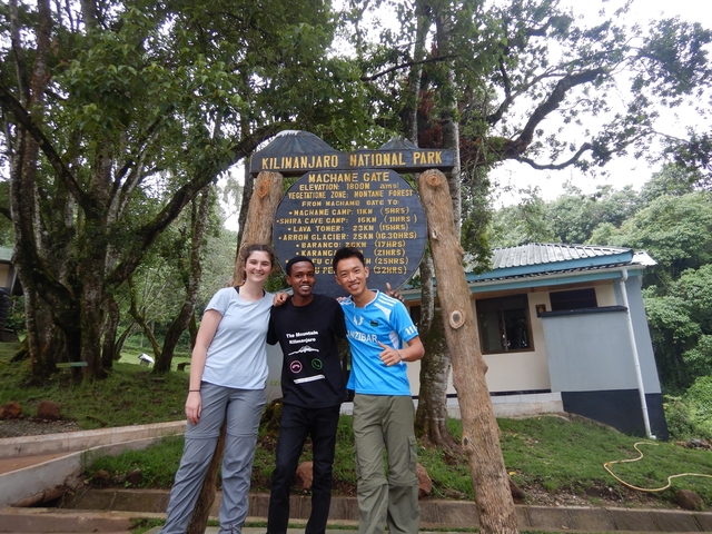       Three people posing at the Kilimanjaro National Park sign.
  
