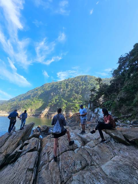 People sitting on rocks with a water body and trees in the background.