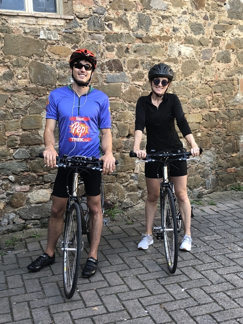 Two cyclists standing in front of a stone wall.