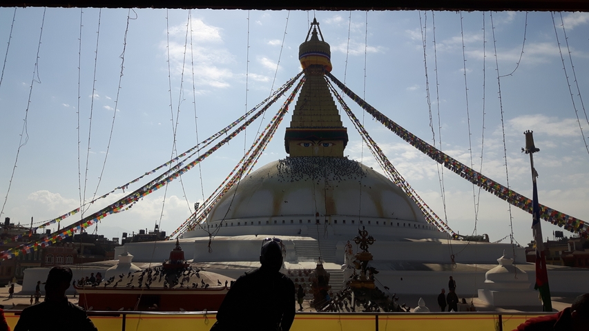       A large stupa with prayer flags and people silhouetted in the foreground.
  