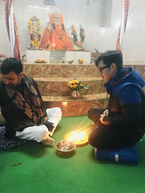       Two people sitting near a ceremonial setup indoors.
  