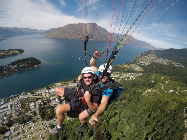       Paragliders soaring over a lake with a mountainous backdrop.
  