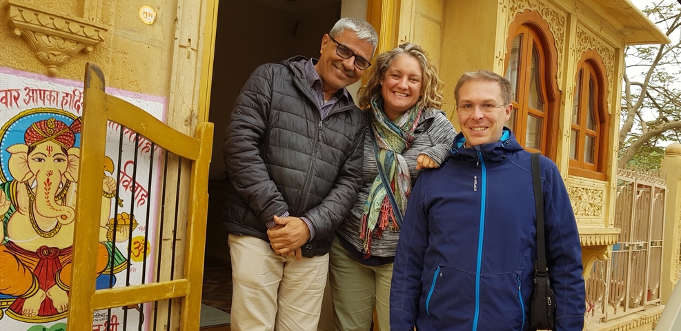 Three people standing together, one of them is an elderly local man.