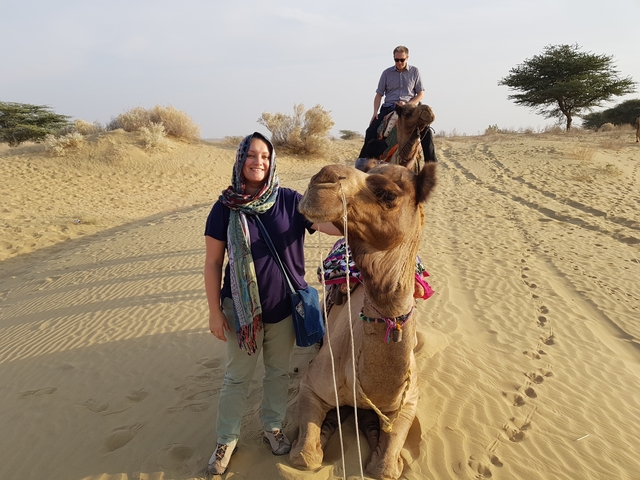       Woman petting a camel in a sandy desert landscape.
  