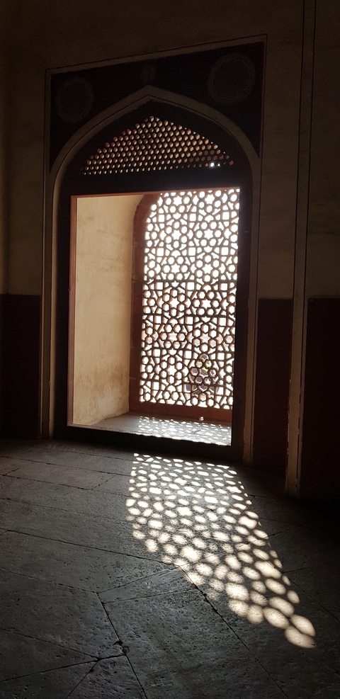       Sunlight filtering through a decorative jali window.
  