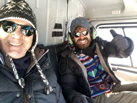       Two men with winter hats inside a helicopter.
  