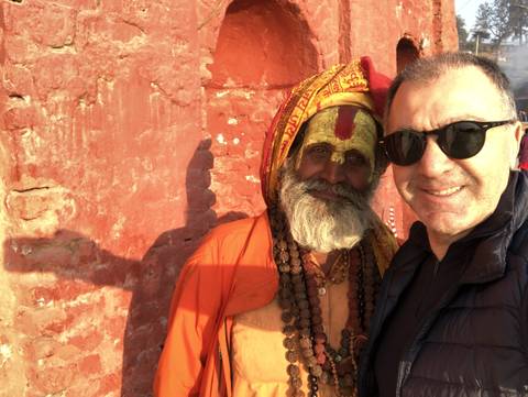       Man taking a selfie with a holy man in traditional attire.
  