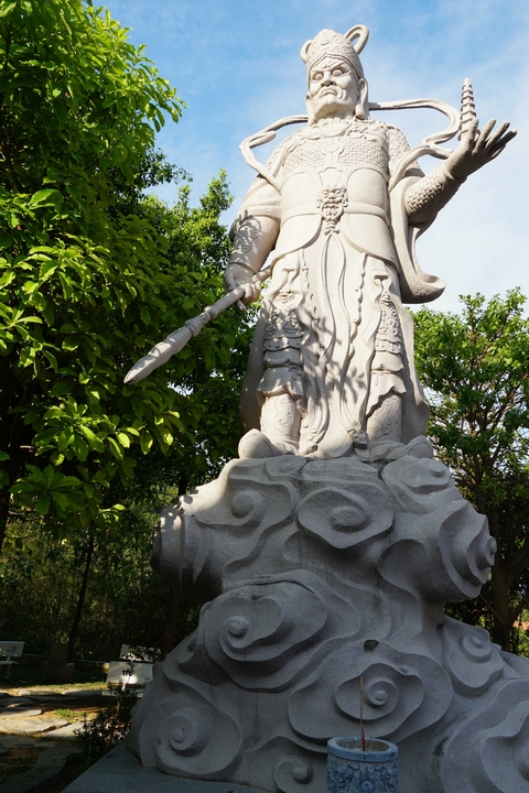 Stone statue partially hidden by green foliage.