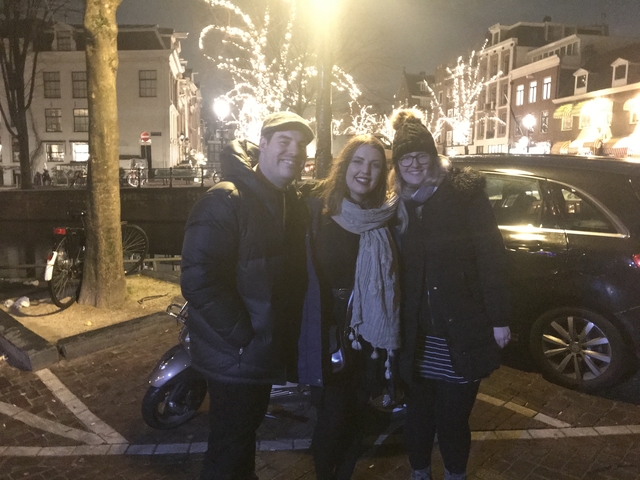 Three people posing on a street with festive lights.