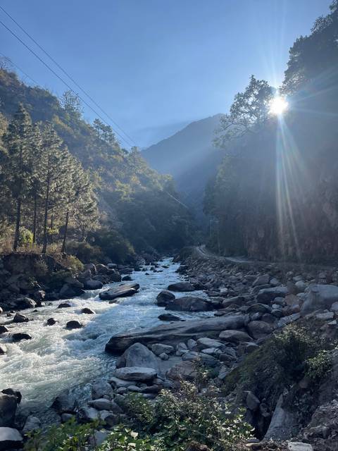 A river with surrounding mountains and trees, with sunlight.