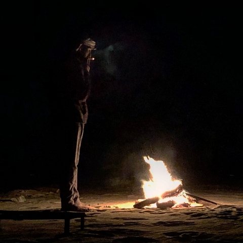 Person standing by a small campfire at night.