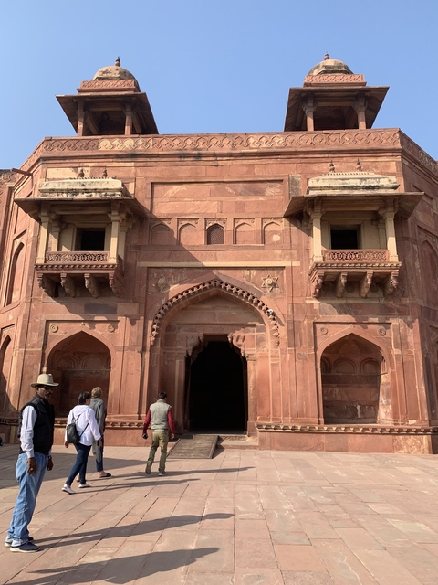 People standing in front of a red sandstone building with intricate designs.