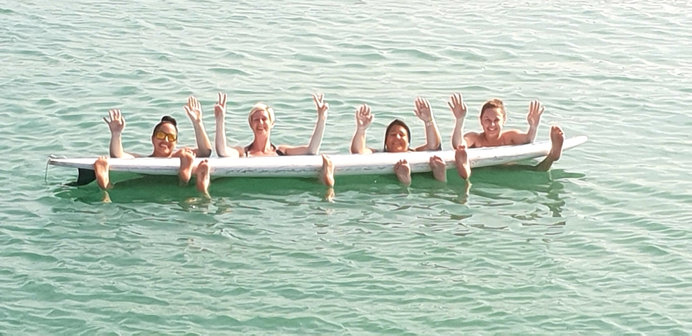 Group of people posing in a line in the water while on a surfboard.