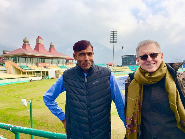       Two men posing in a stadium with mountains in the background.
  