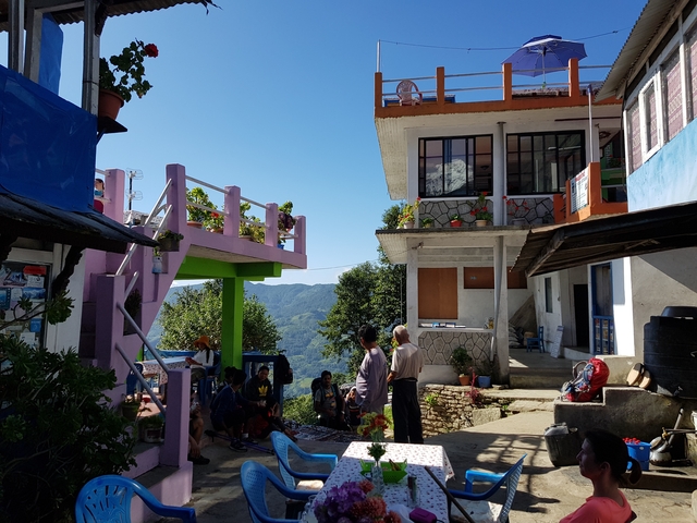 People interacting in a courtyard with colorful buildings and distant mountains.