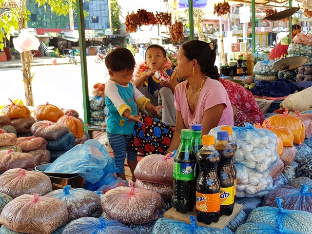       A family at a local market surrounded by bags of goods and food products.
  