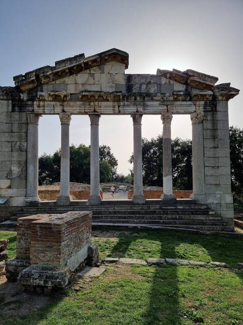 Ancient ruins with columns standing in a grassy area.