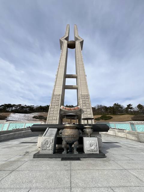       Tall monument with traditional carvings under a grey sky.
  