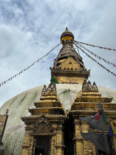       Golden spire with prayer flags and a clouded sky.
  