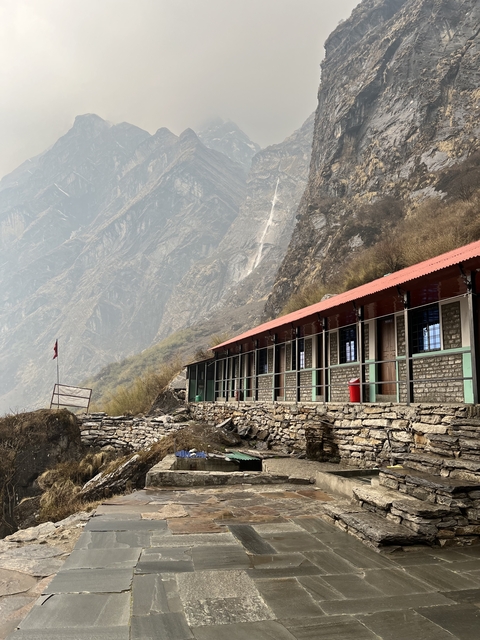 Building with stone walls set against a mountain backdrop.