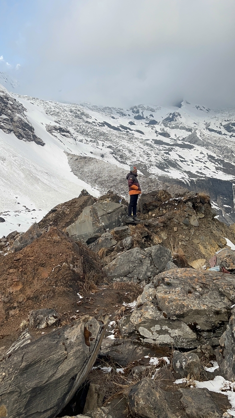 Person standing on rocky terrain with snowy mountains.