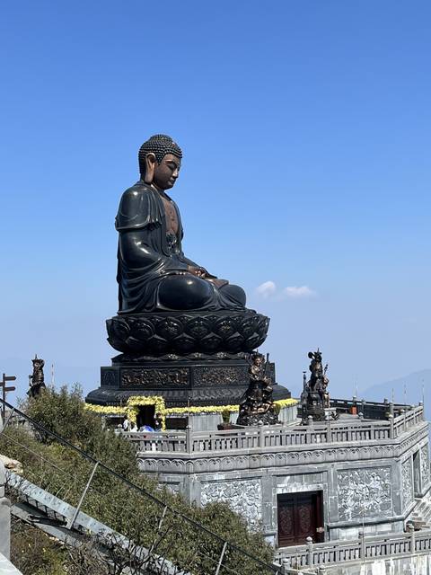 A large statue of a seated figure on a pedestal outdoors.