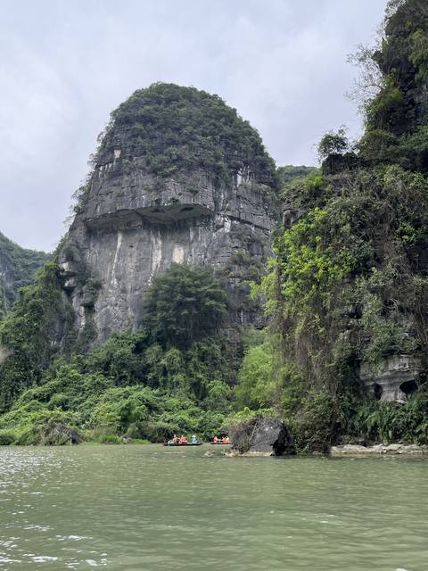       A large rocky hill with small boats on a river.
  