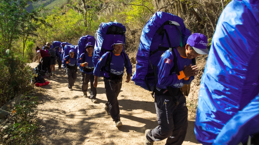       Group of porters carrying large backpacks on a trail.
  