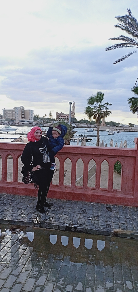 Woman with a child beside a river, with a cityscape in the distance.