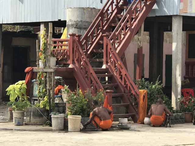       Two people wearing orange garments sitting on a stone patio with flowers.
  