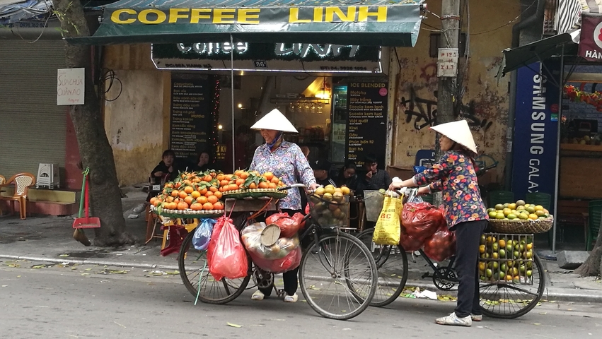 Two women selling fruits on bicycles in an urban area.