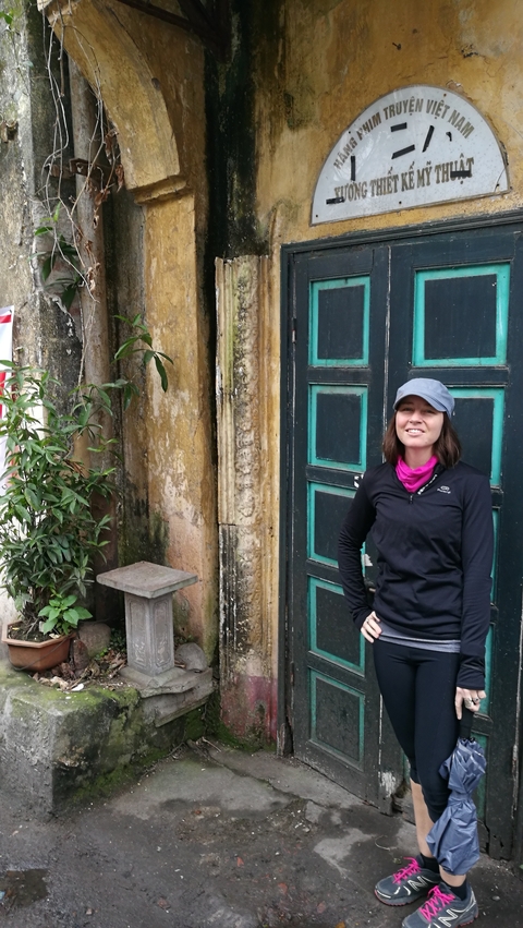 A woman in a hat standing next to a weathered wall.