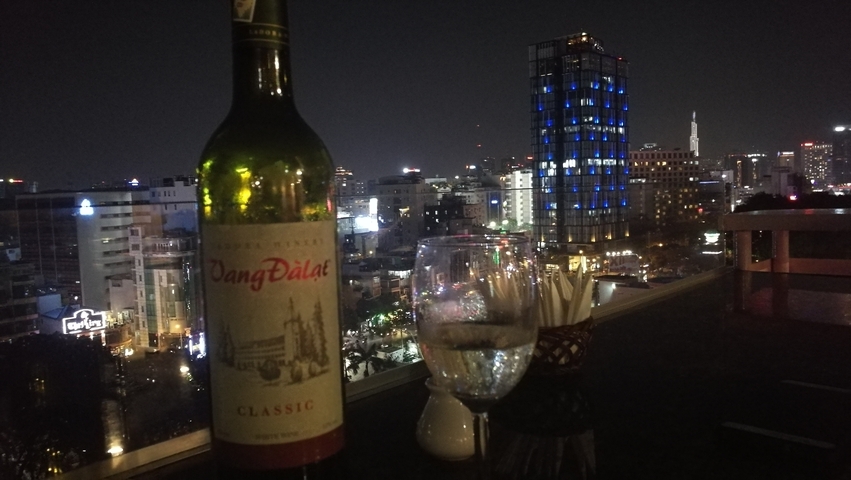 Night view of a cityscape with a bottle and glass in the foreground.