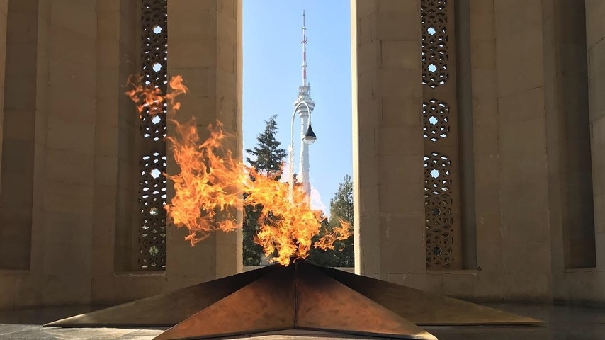       Memorial flame with a view of a distant tower.
  