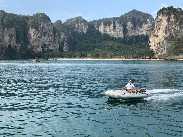 A person riding a motorboat with cliffs in the background.