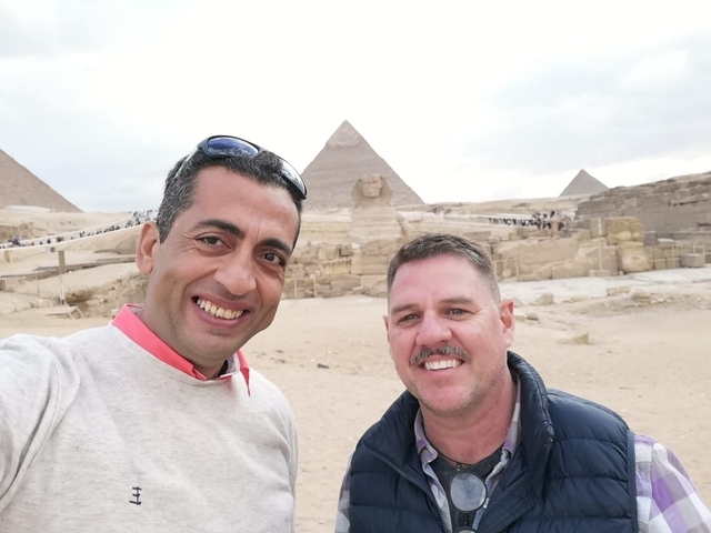       Two people taking a selfie with pyramids and the Sphinx in the background.
  